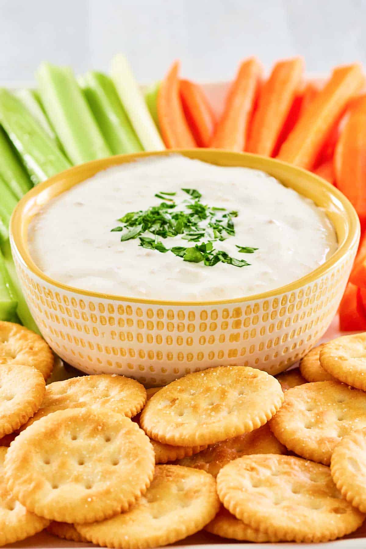 New England clam chowder dip on a platter with crackers, celery, and carrots.