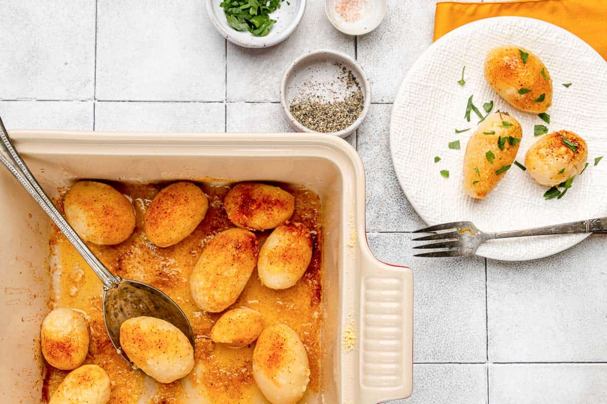Overhead view of golden potatoes in a baking dish and on a plate.