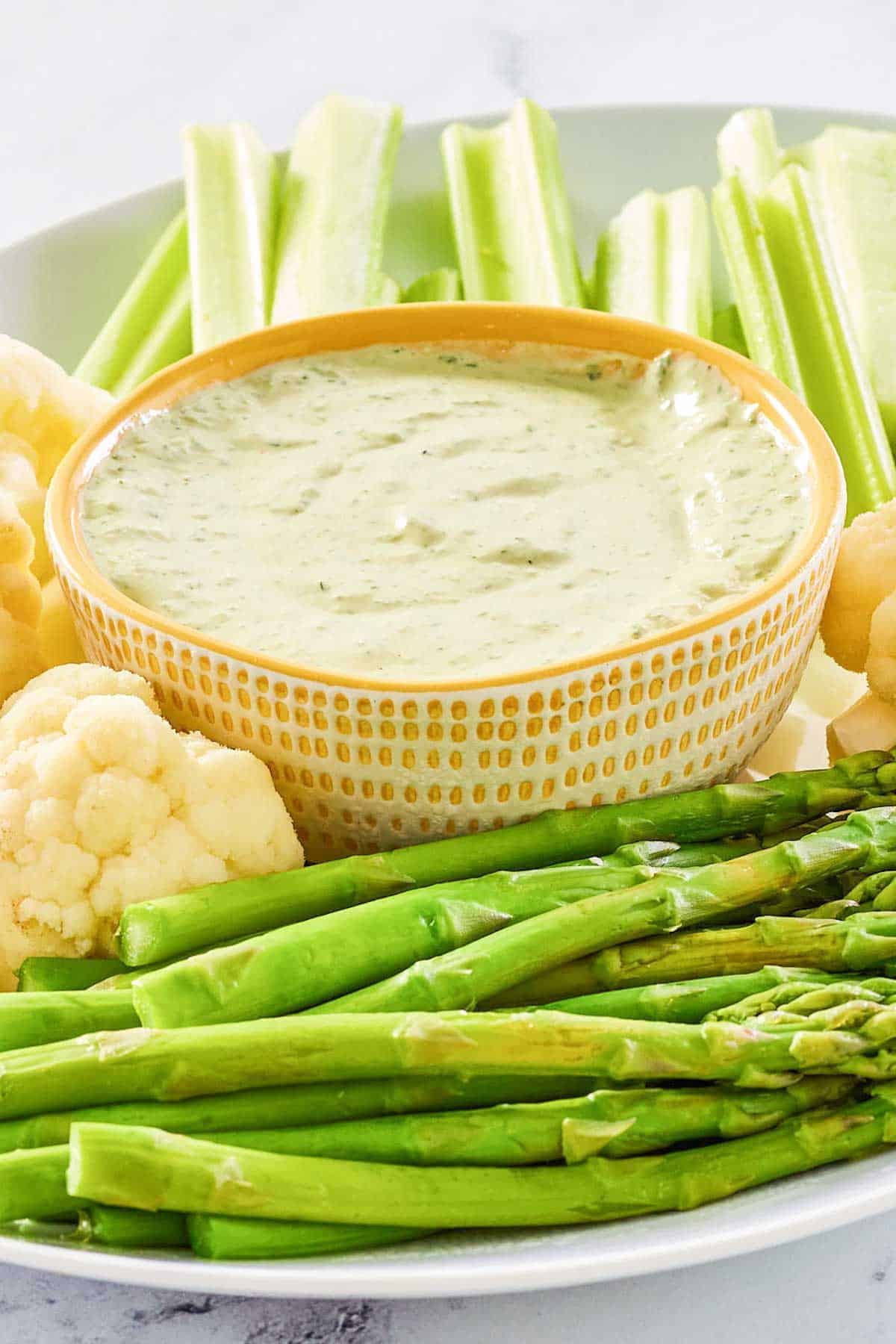 Green goddess dip in a bowl with vegetables around it on a platter.
