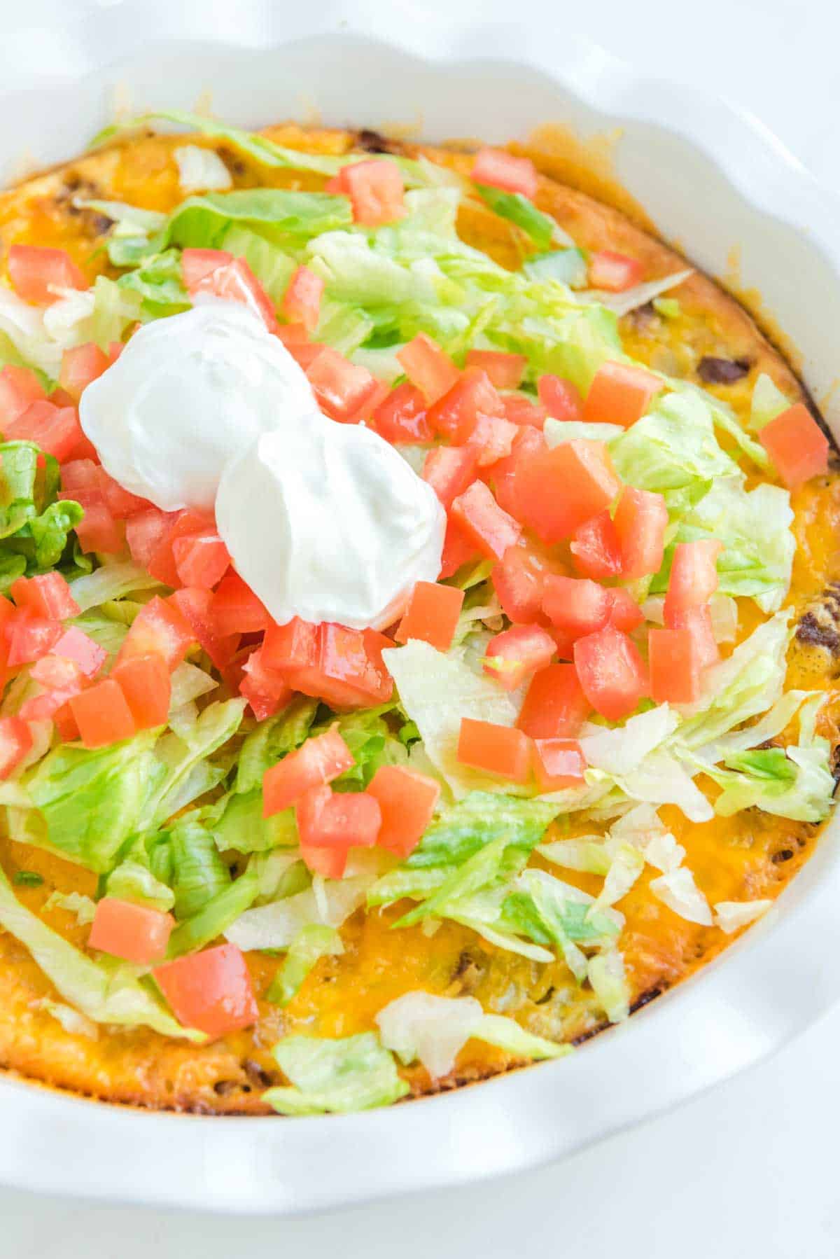 Impossible taco pie topped with lettuce, chopped tomatoes, and sour cream.