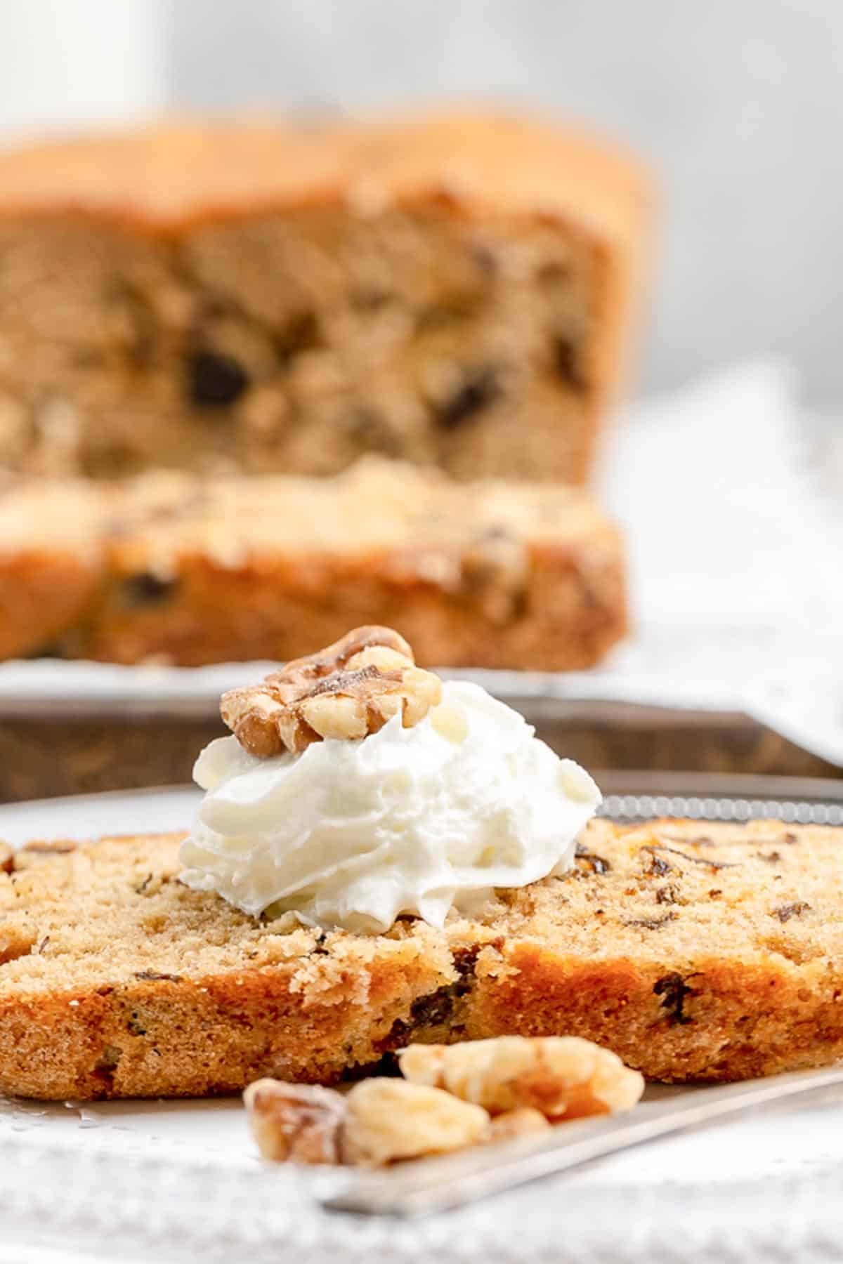 Closeup of a slice of prune cake topped with whipped cream and a walnut.