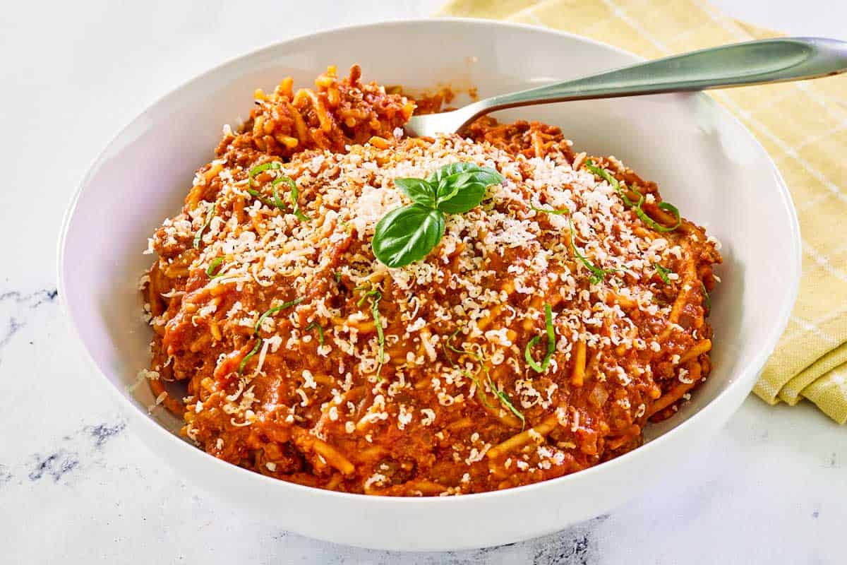 Skillet spaghetti garnished with parmesan cheese and fresh basil.