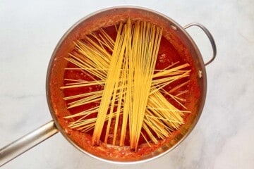 Adding spaghetti pasta to meat sauce in a skillet.