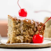 A slice of sour cream cherry coffee cake with glaze and cherries on a plate.