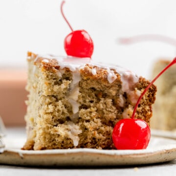 A slice of sour cream cherry coffee cake with glaze and cherries on a plate.
