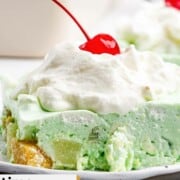 Lime jello salad slice topped with whipped cream and a cherry.