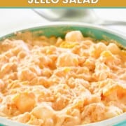 Orange Jello salad with cottage cheese and marshmallows in a green bowl.