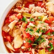 A bowl of cabbage and sausage soup with tomatoes.