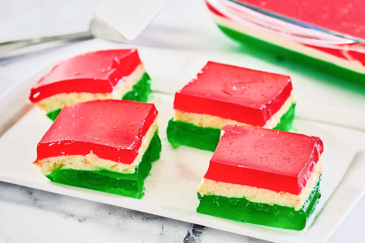 Four servings of Christmas ribbon jello salad on a plate and the dish behind it.