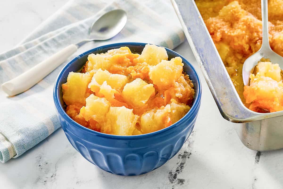 A bowl of pineapple cheese casserole next to the casserole dish.