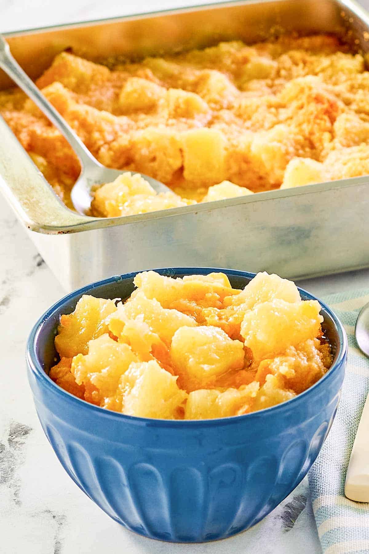 Pineapple cheese casserole in a square baking dish and a serving in a bowl.