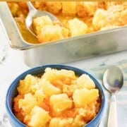 A bowl of pineapple cheese casserole, a spoon, and the casserole in a baking dish.