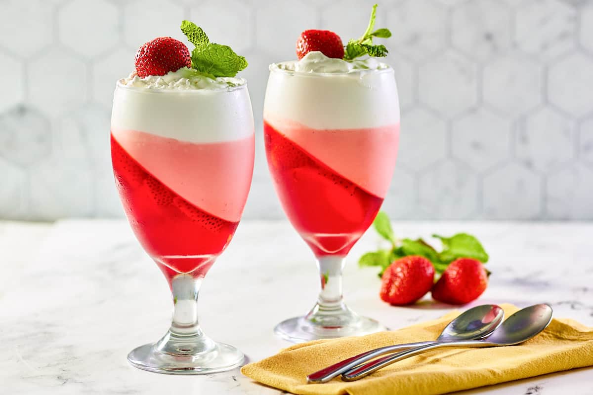Strawberry jello parfait in two glasses, two spoons, and two fresh strawberries.