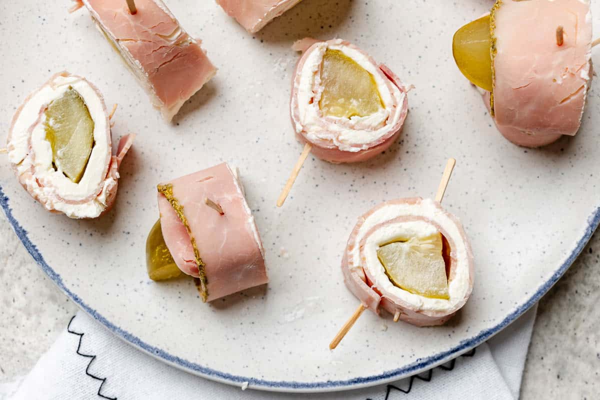 Ham and pickle roll ups scattered on a plate.