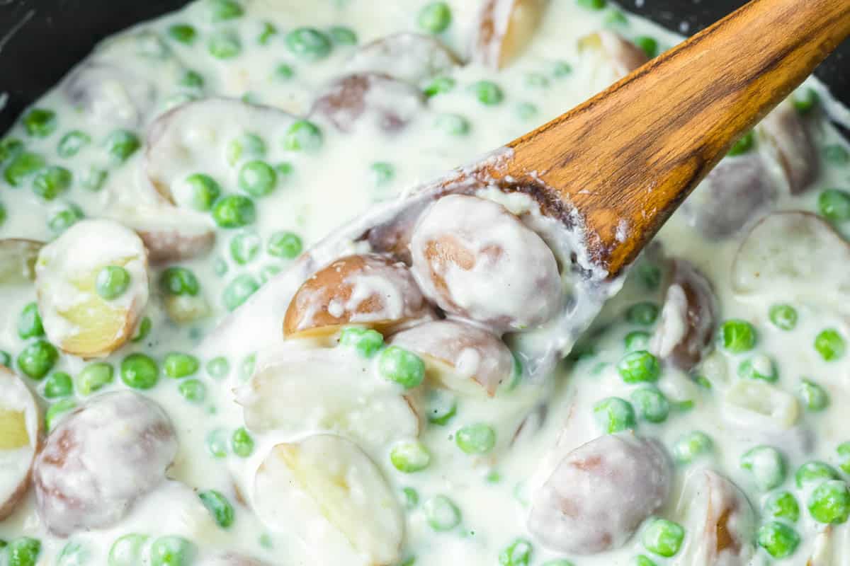 Creamed peas and potatoes on a wooden spoon in a skillet.