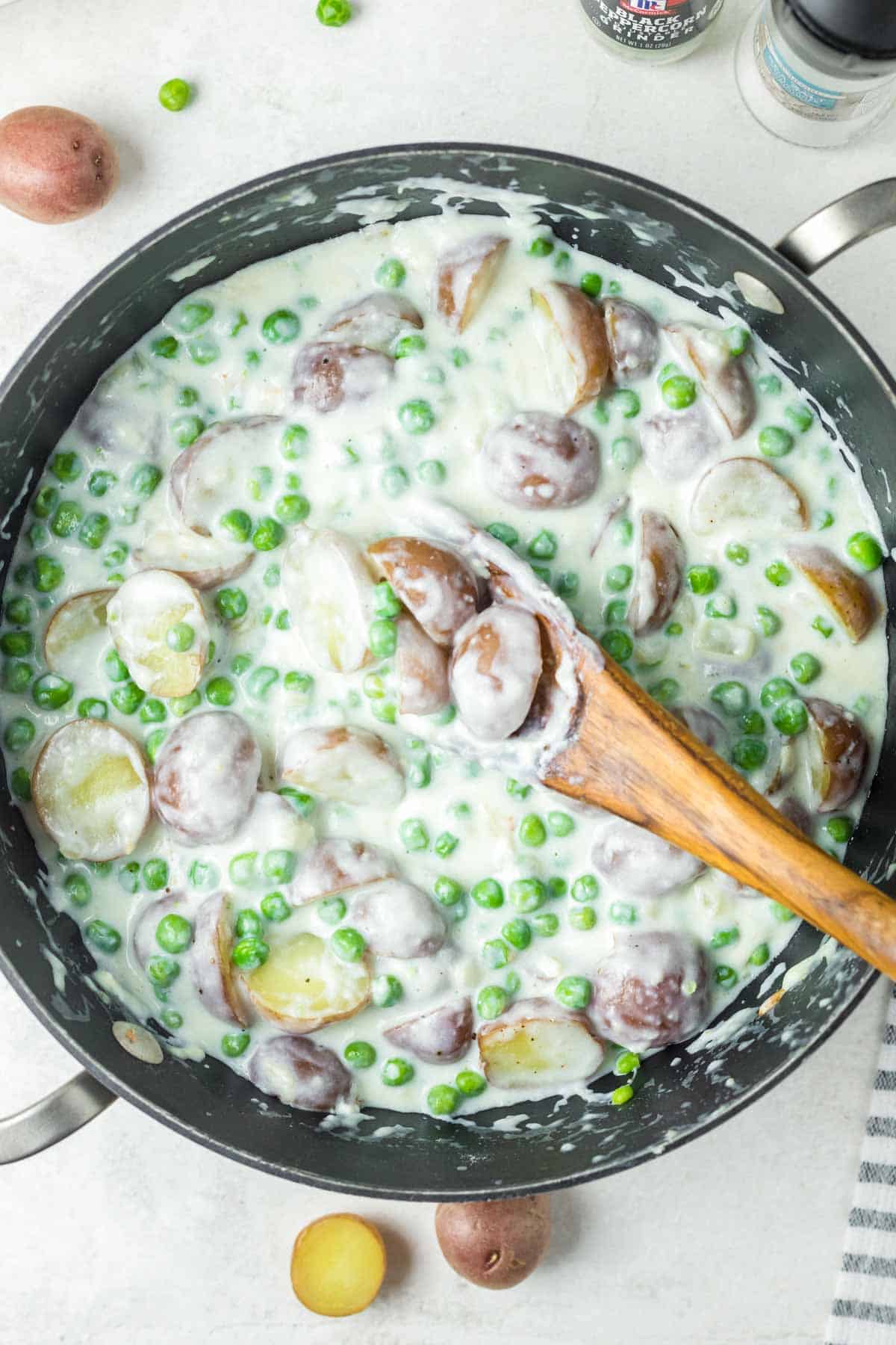 Creamed peas and potatoes in a skillet on a marble surface.