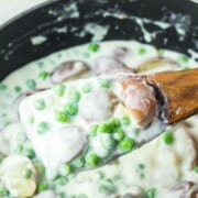 Creamed peas and potatoes on a wooden spoon over a skillet of it.