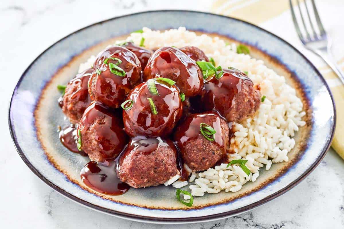 Sweet and sour meatballs and rice on a dinner plate.