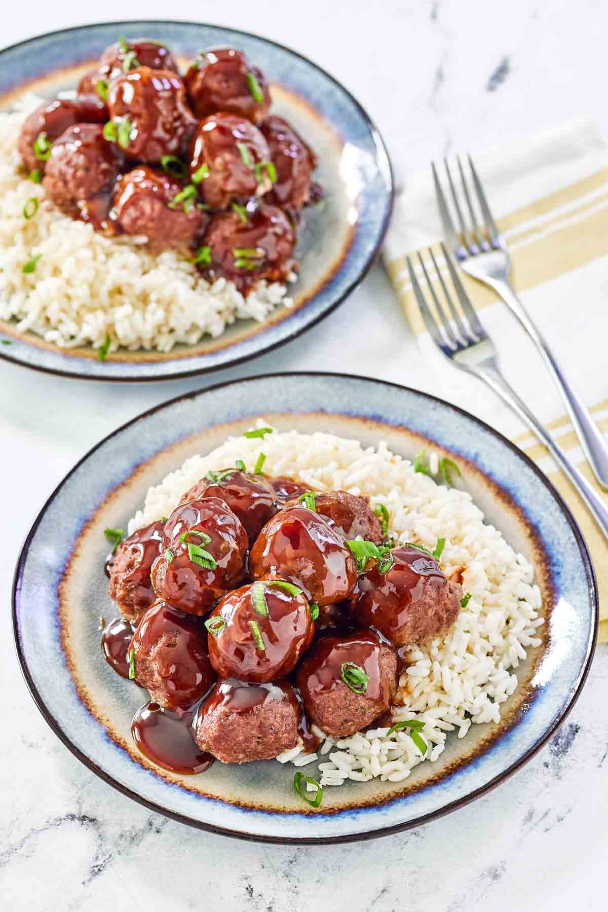 Sweet and sour meatballs over butter rice on two plates.